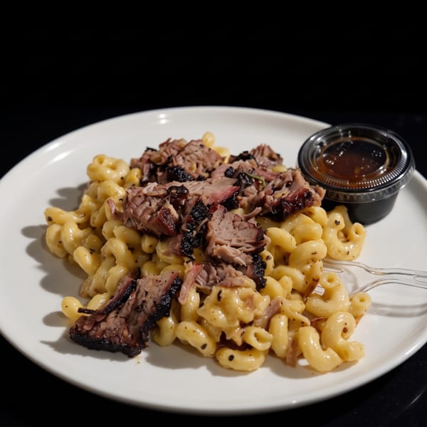 Creamy mac and cheese topped with sliced brisket, a small sauce cup, and a plastic fork.