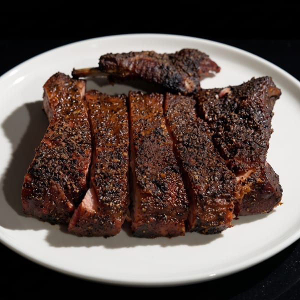 Sliced, dark-crusted steak with a pink interior, presented on a white plate.
