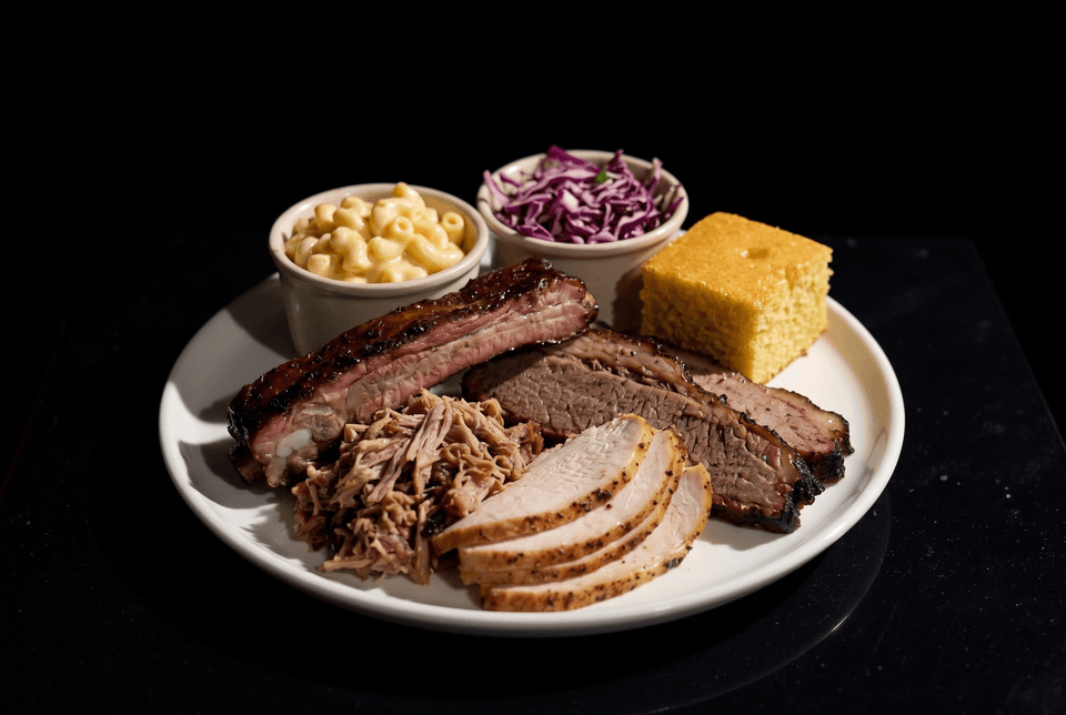 Plate of BBQ ribs, brisket, pulled pork, turkey, mac and cheese, coleslaw, and cornbread.